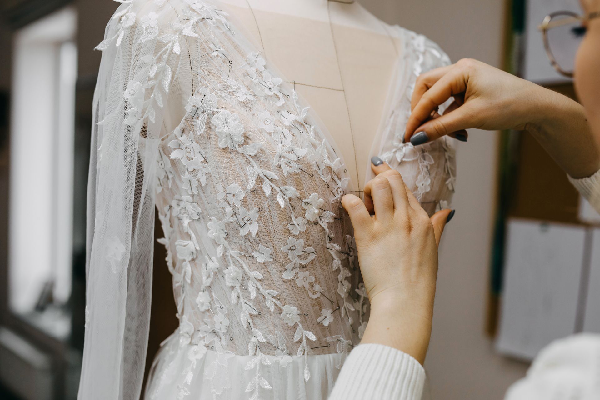 Hands fastening a lace wedding dress on a mannequin in a fitting room