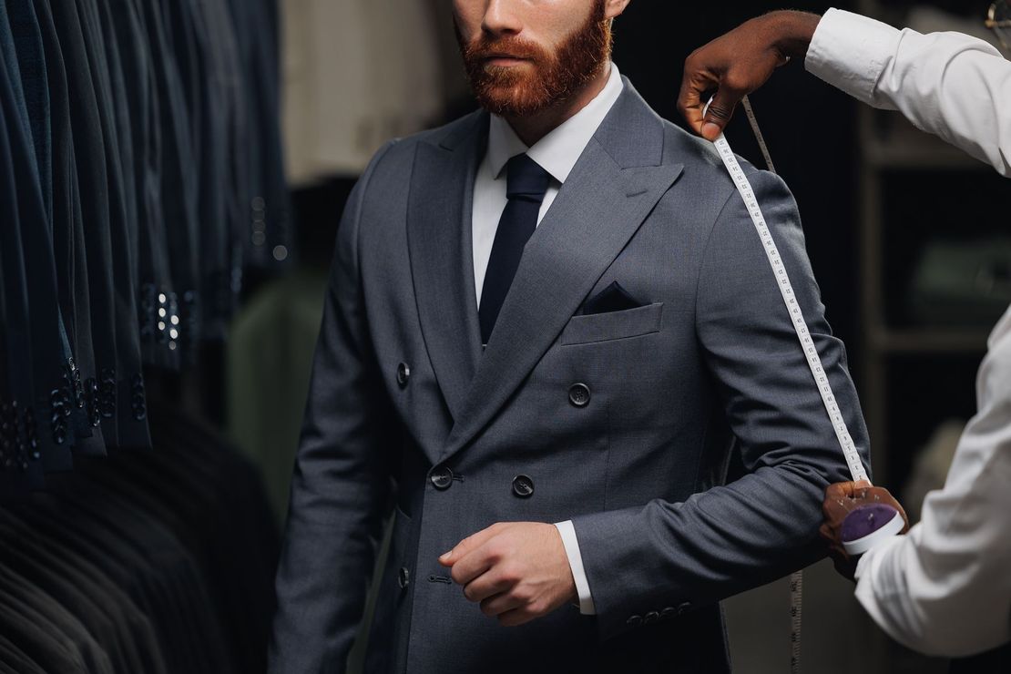 Tailor adjusting tape on a man in a gray suit in a fitting room