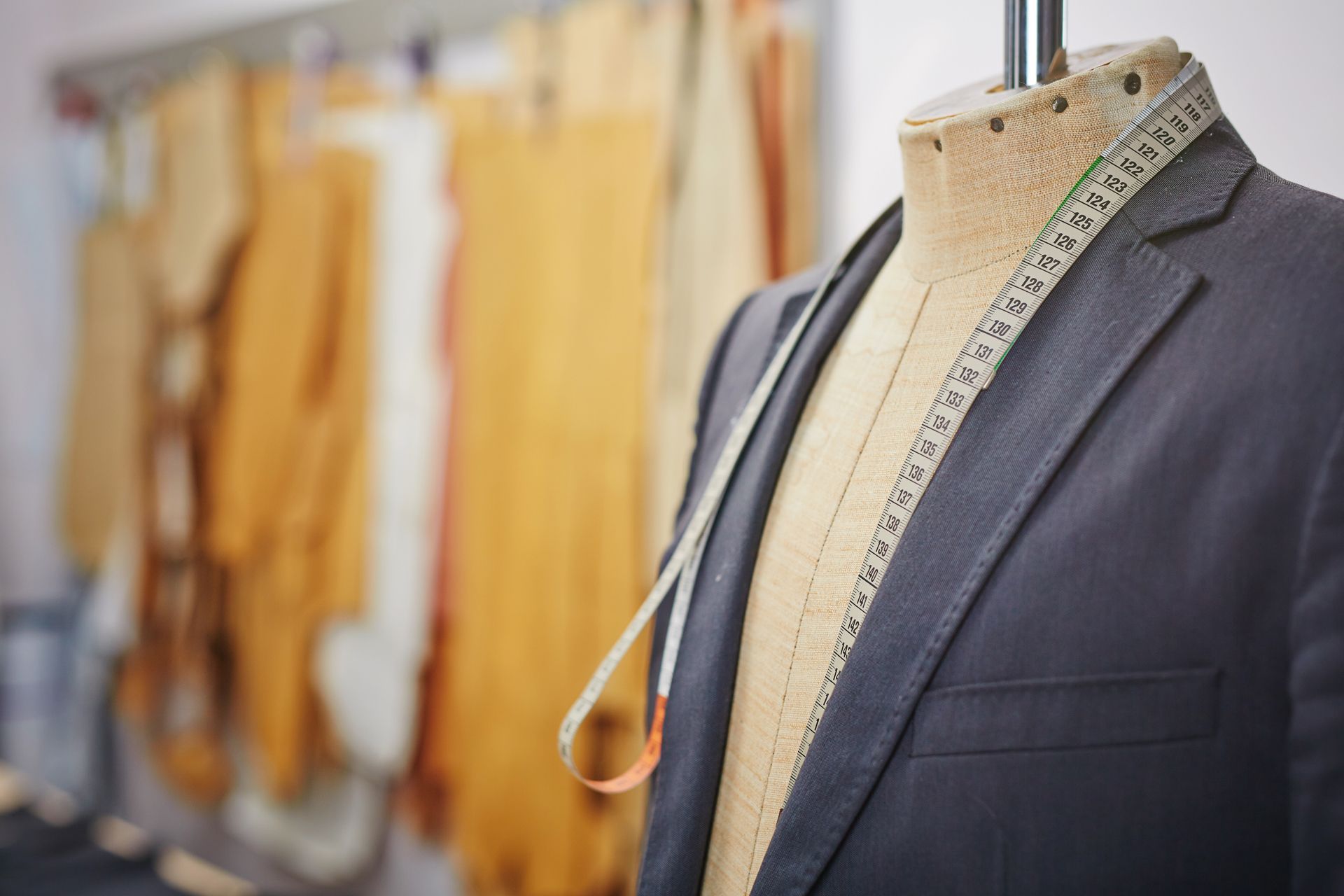 Tailor’s mannequin in a suit jacket with measuring tape, beside hanging garments in a sewing studio