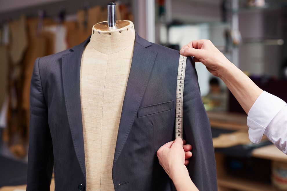 Tailor measuring a dark gray suit jacket on a dress form with a tape measure