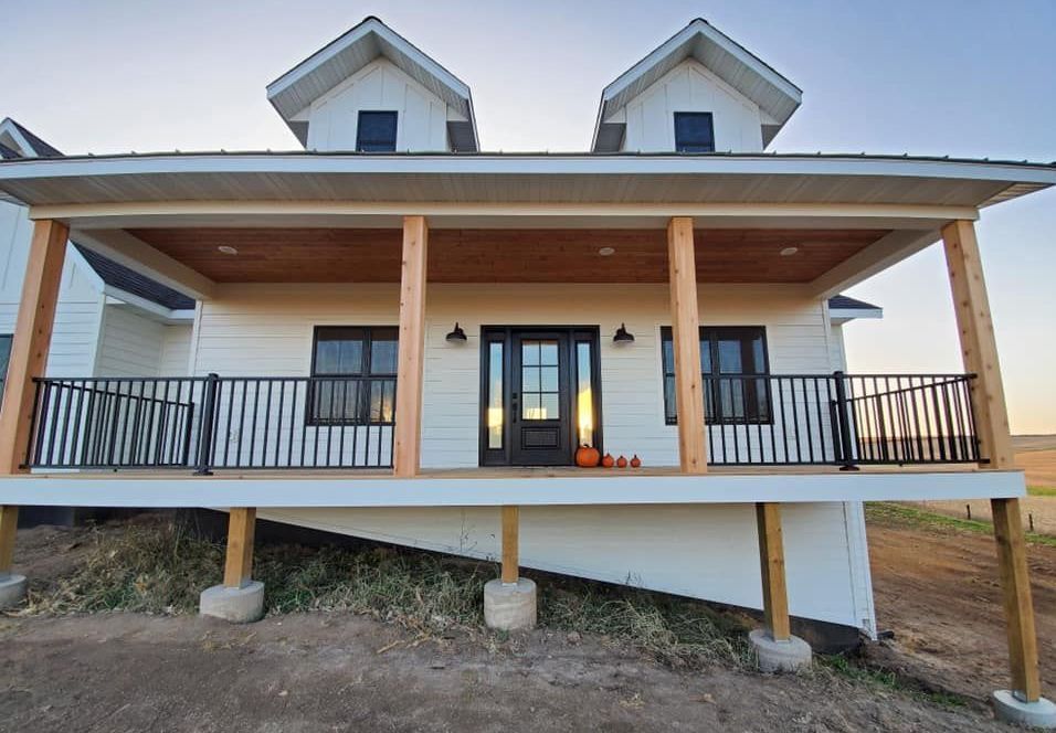 A white house with a large porch and a black railing.