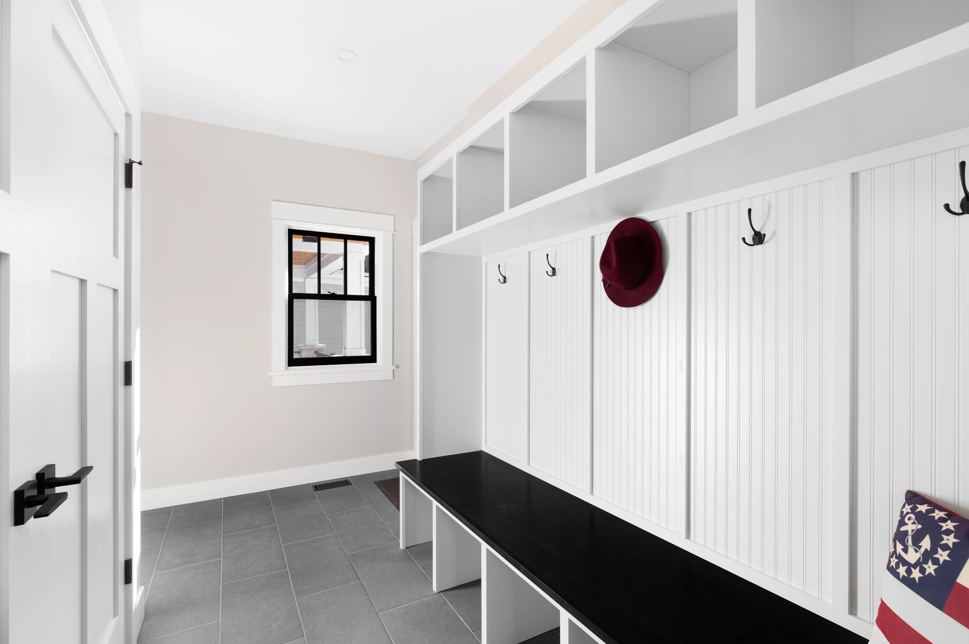 White mudroom with black bench, cubbies, and coat hooks; a window and door.
