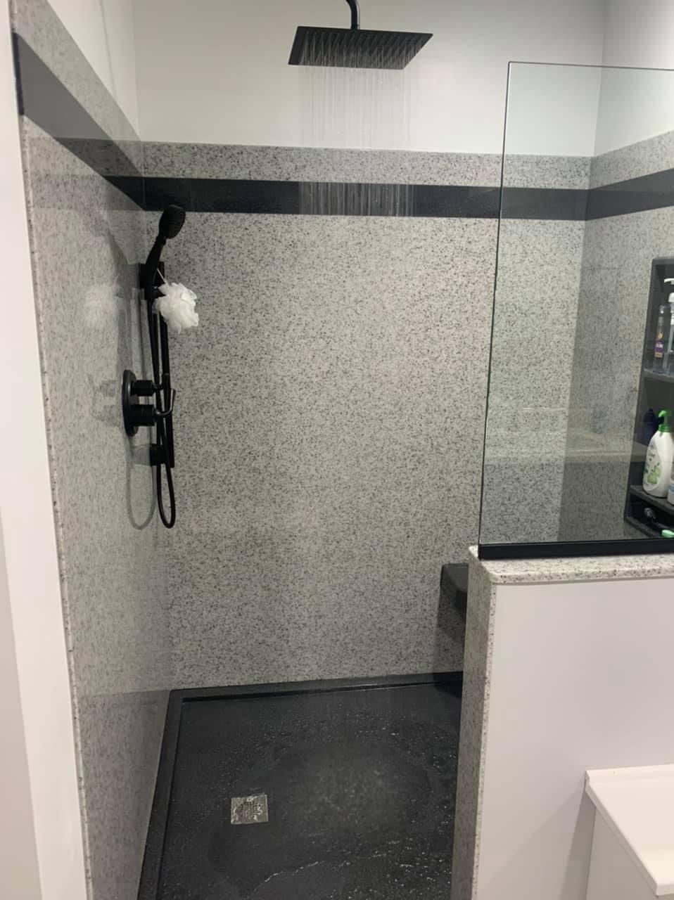 Walk-in shower remodel with granite-look walls, rainfall showerhead, glass panel, and built-in seating