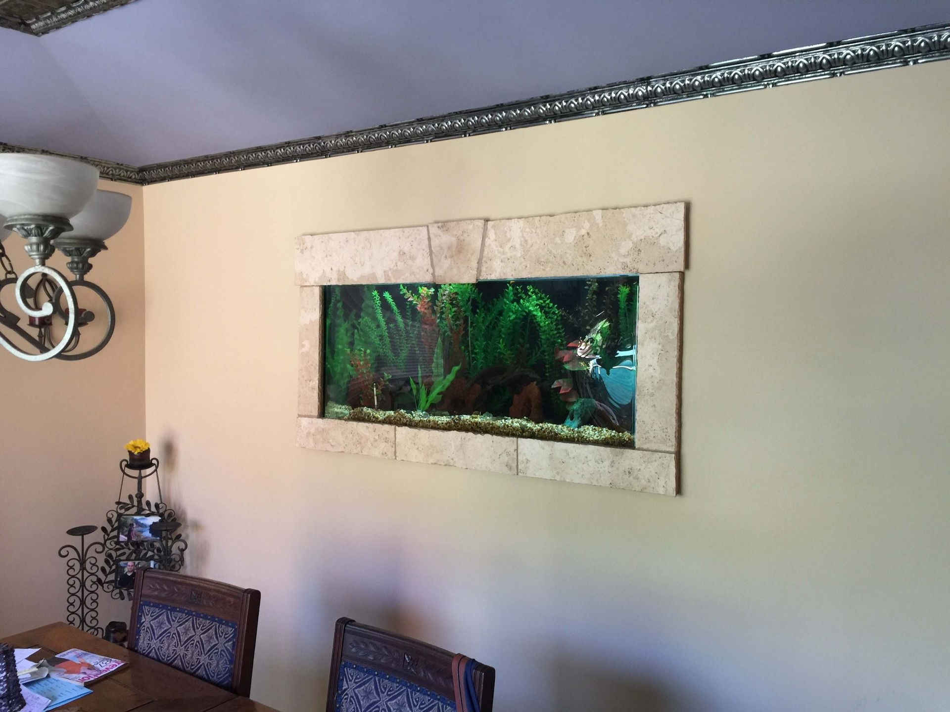 A large aquarium is hanging on a wall in a dining room.