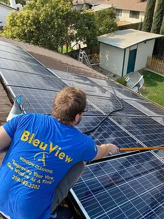 A man in a blue shirt is cleaning solar panels on a roof.