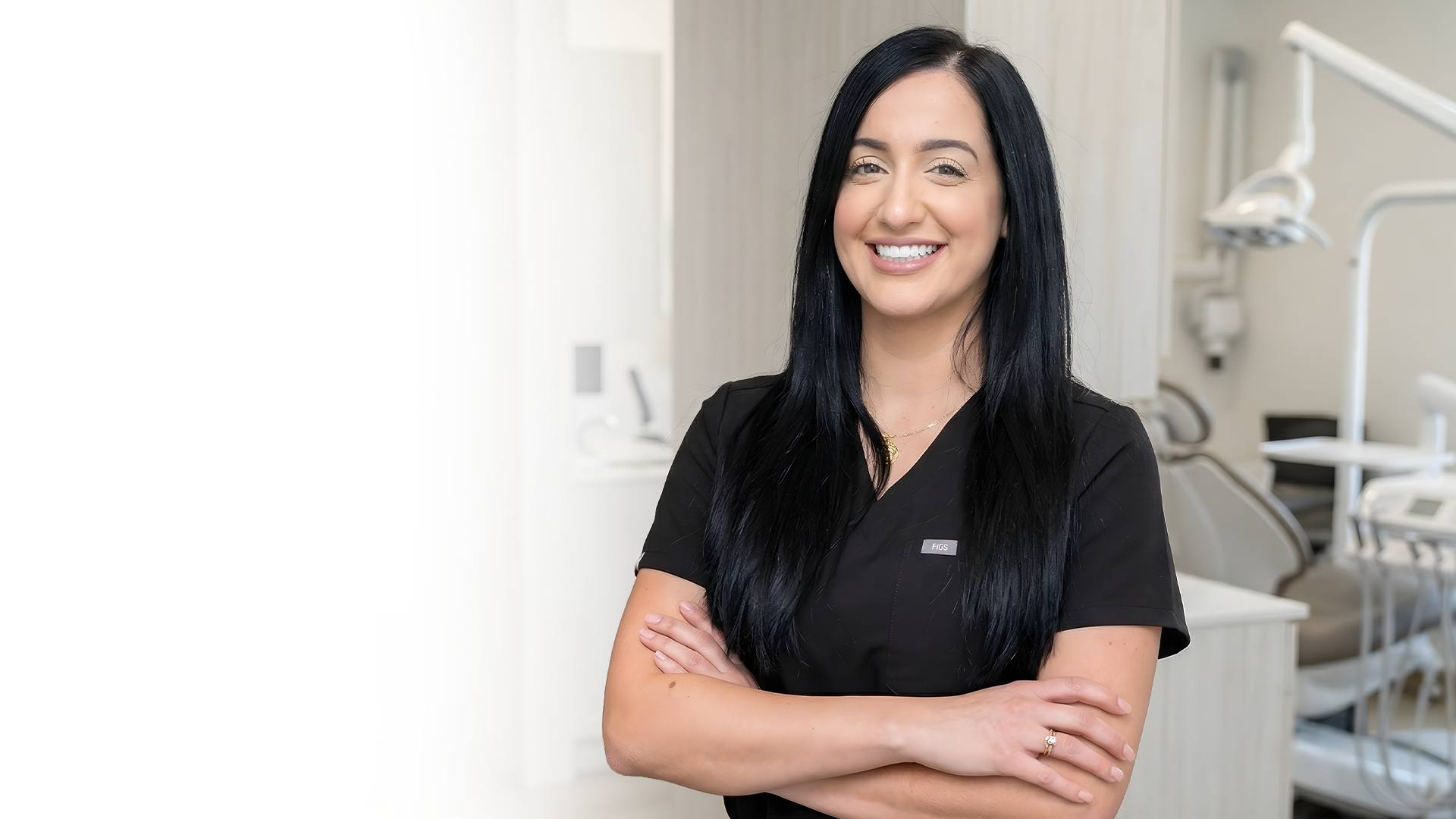 Woman in black scrubs smiling with arms crossed in a bright dental office