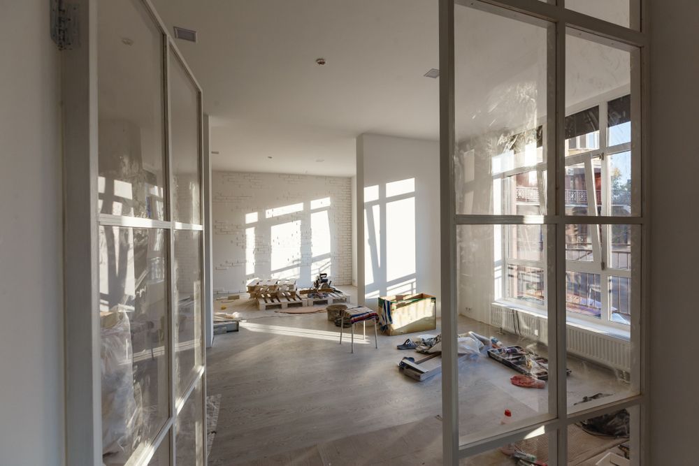 Interior view of an apartment under renovation with glass paneled doors and bright sunlight.