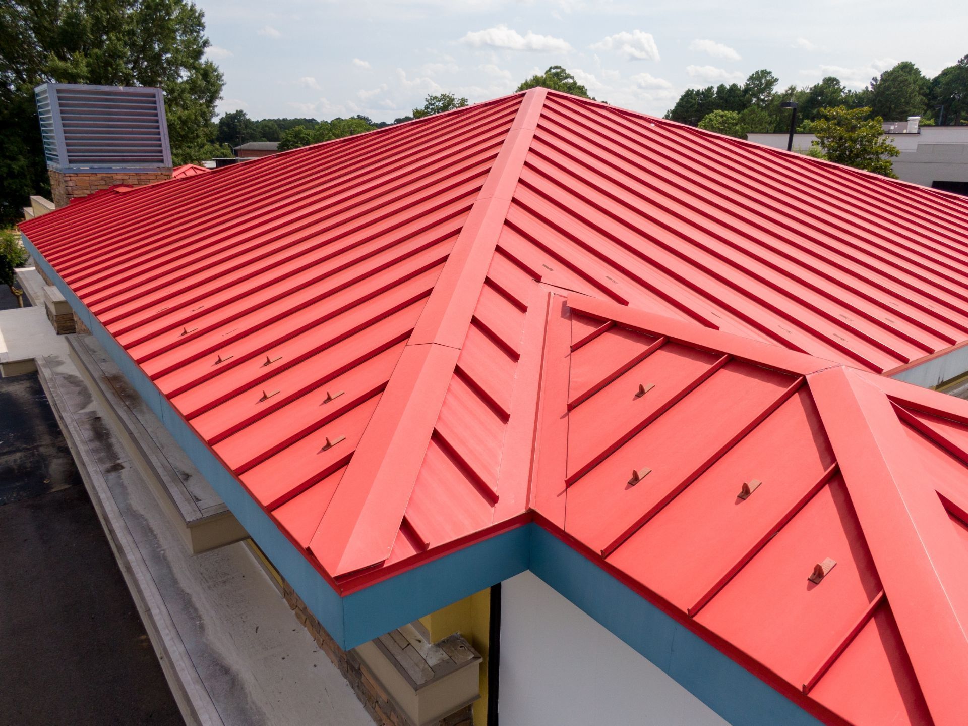 Red metal roof on a building with a light blue trim, on a sunny day.