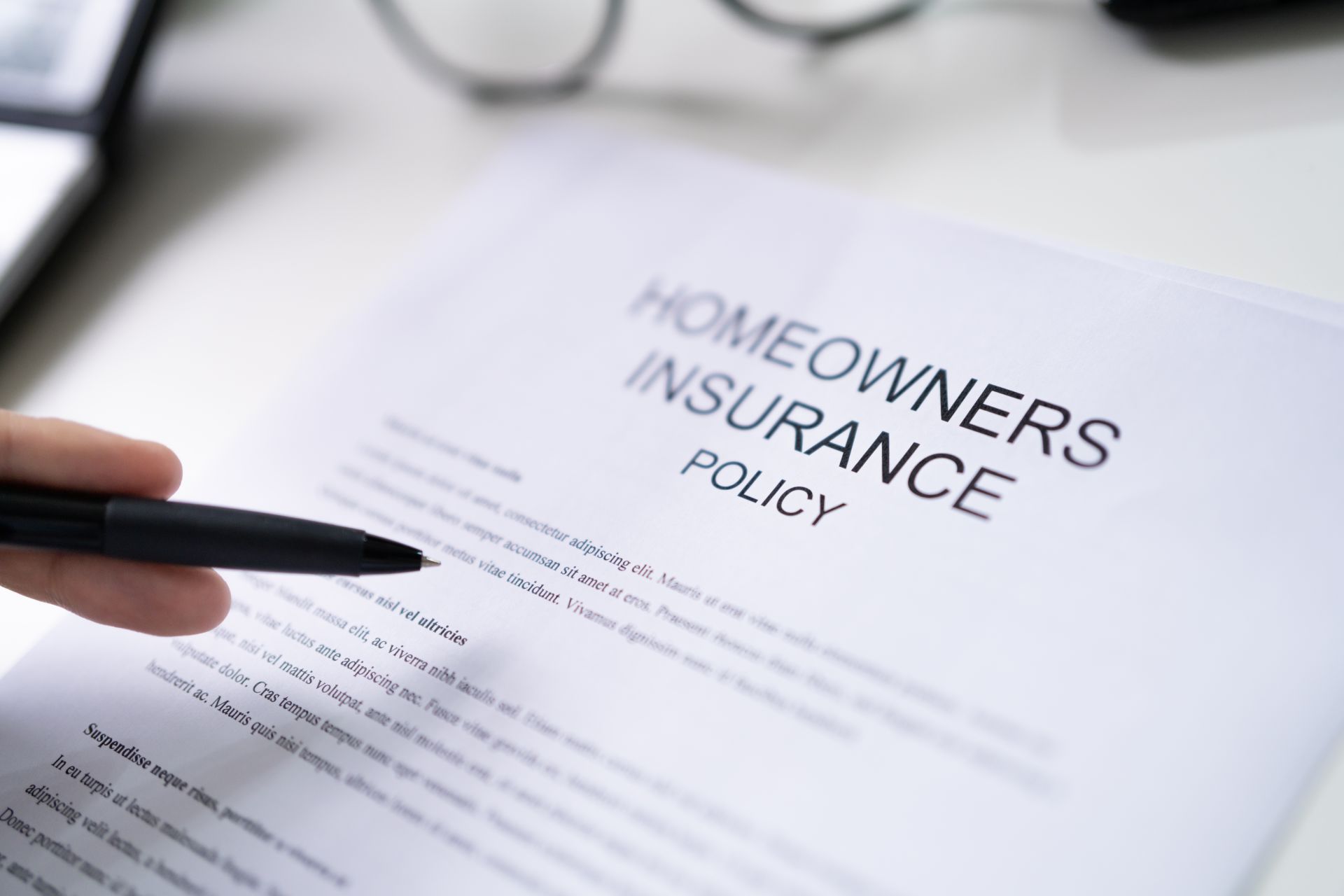 Person pointing a pen at a homeowners insurance policy document on a white desk.