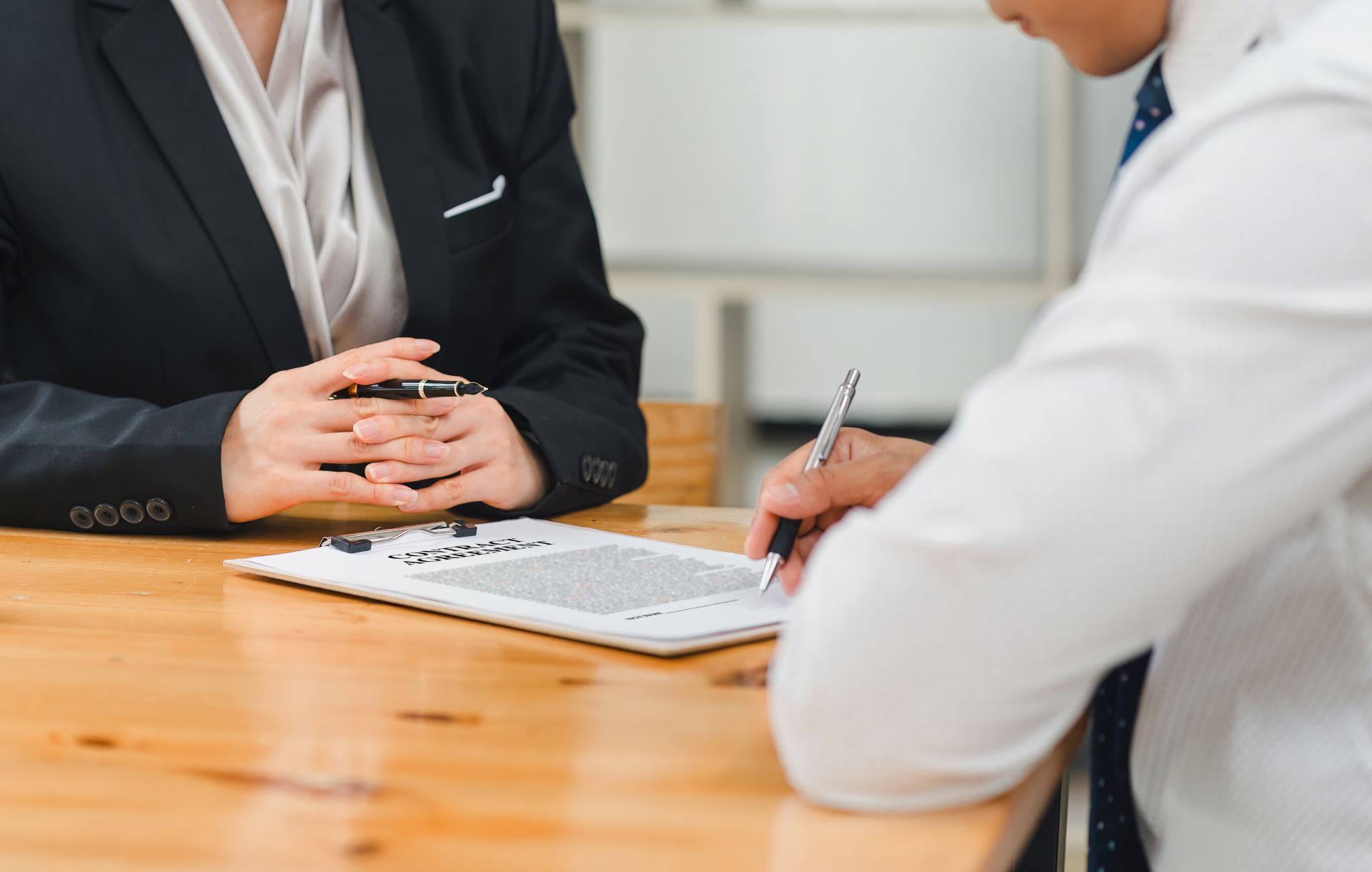 Person in suit across table from person signing document.