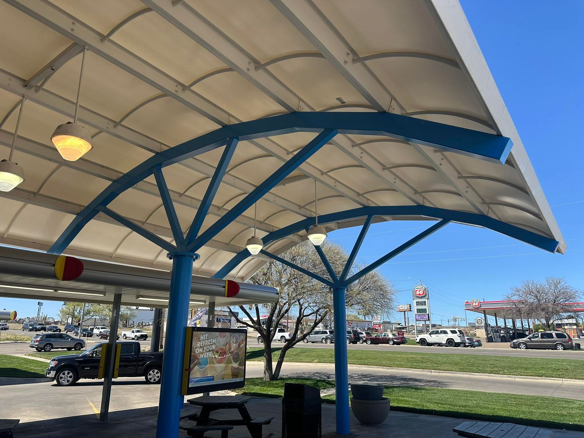 Blue-framed canopy with off-white covering. Drive-in restaurant, blue poles and trim, street view with cars and blue sky.