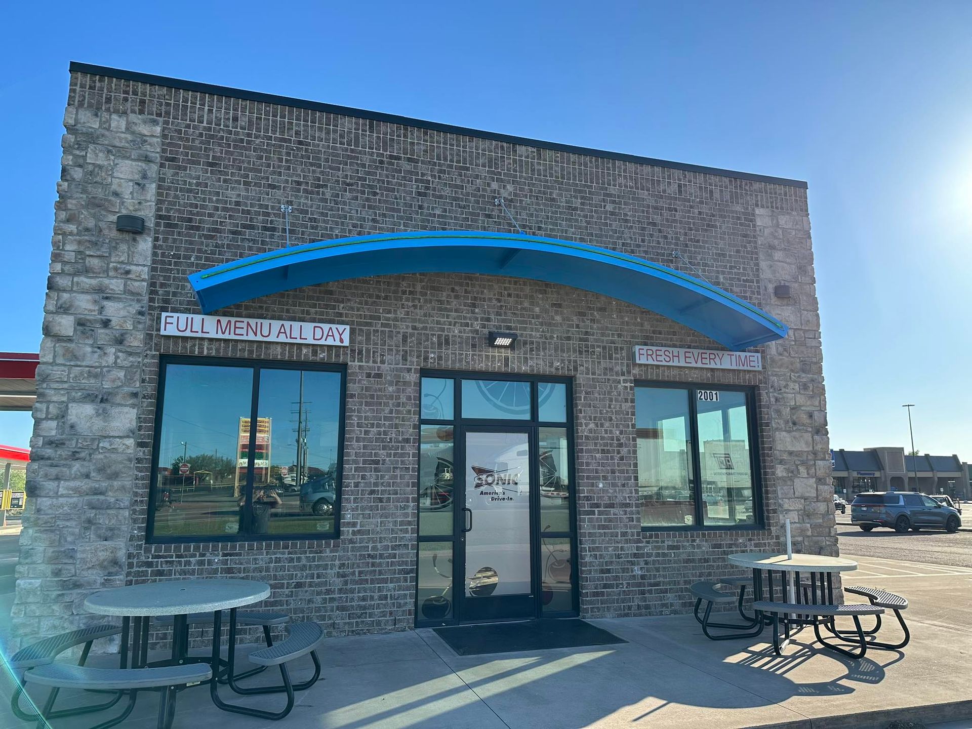 A brick building with blue awning, tables, and reflective windows.