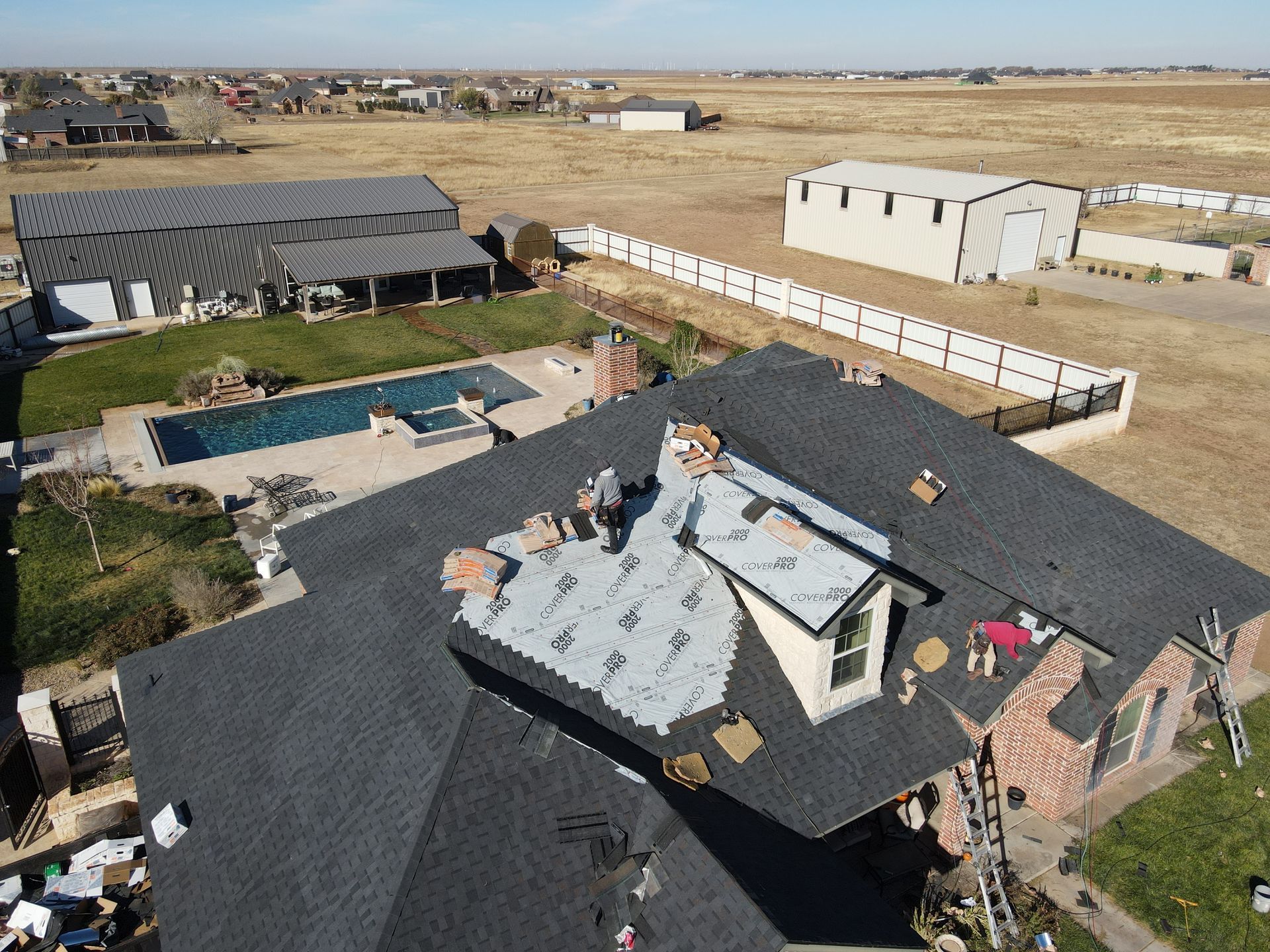 Aerial view of a home with a roof under repair; workers on the roof, partially covered with shingles.