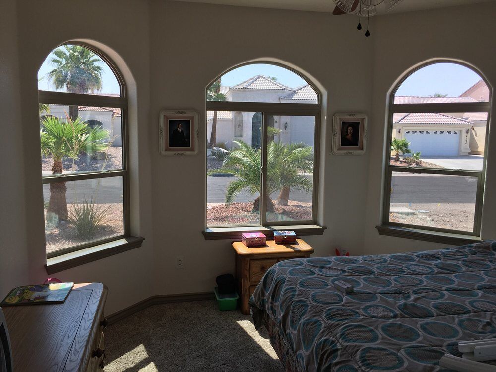 Bedroom with arched windows overlooking a street; bed, nightstand, and dresser are visible.