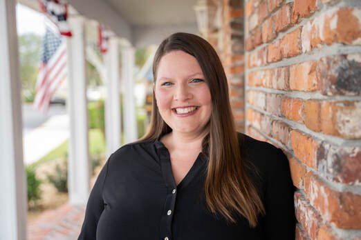 A woman is standing in front of a brick wall and smiling.