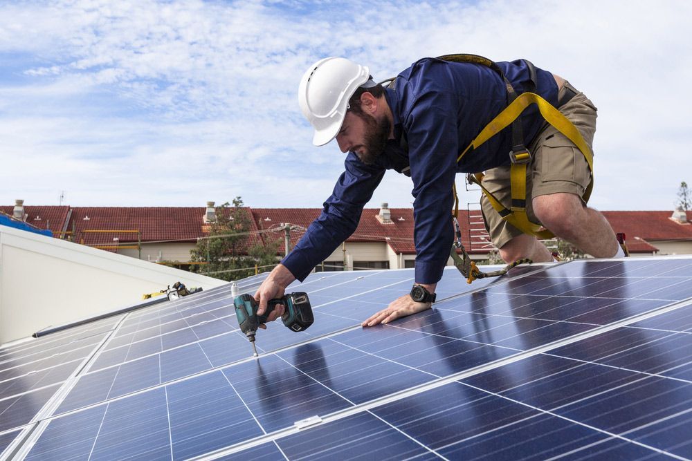 Man Is Installing Solar Panels On The Roof Of A Building — Max Fox Electrical in Armidale, NSW
