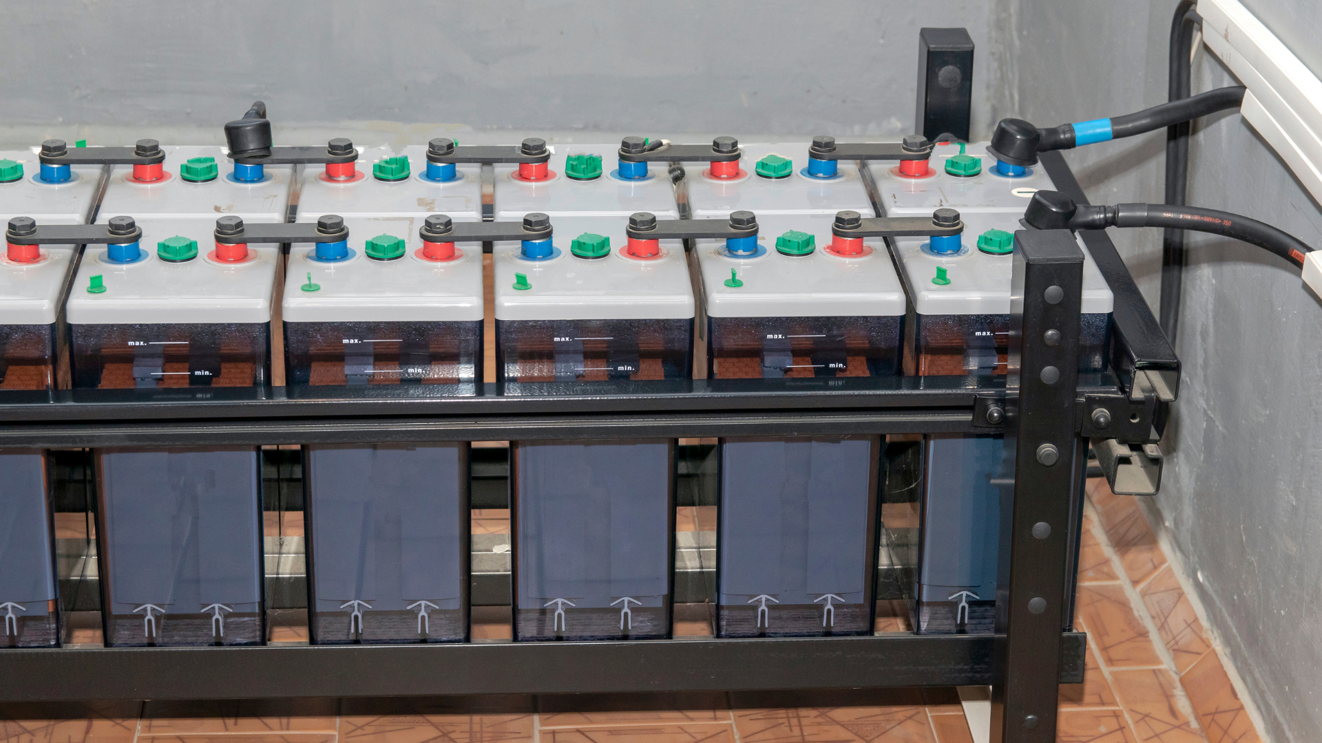 A rack of large, rectangular industrial batteries with blue and red terminal caps, connected by thick black cables.