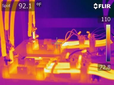 A thermal infrared image showing electrical components, with bright yellow and orange areas indicating heat intensity.