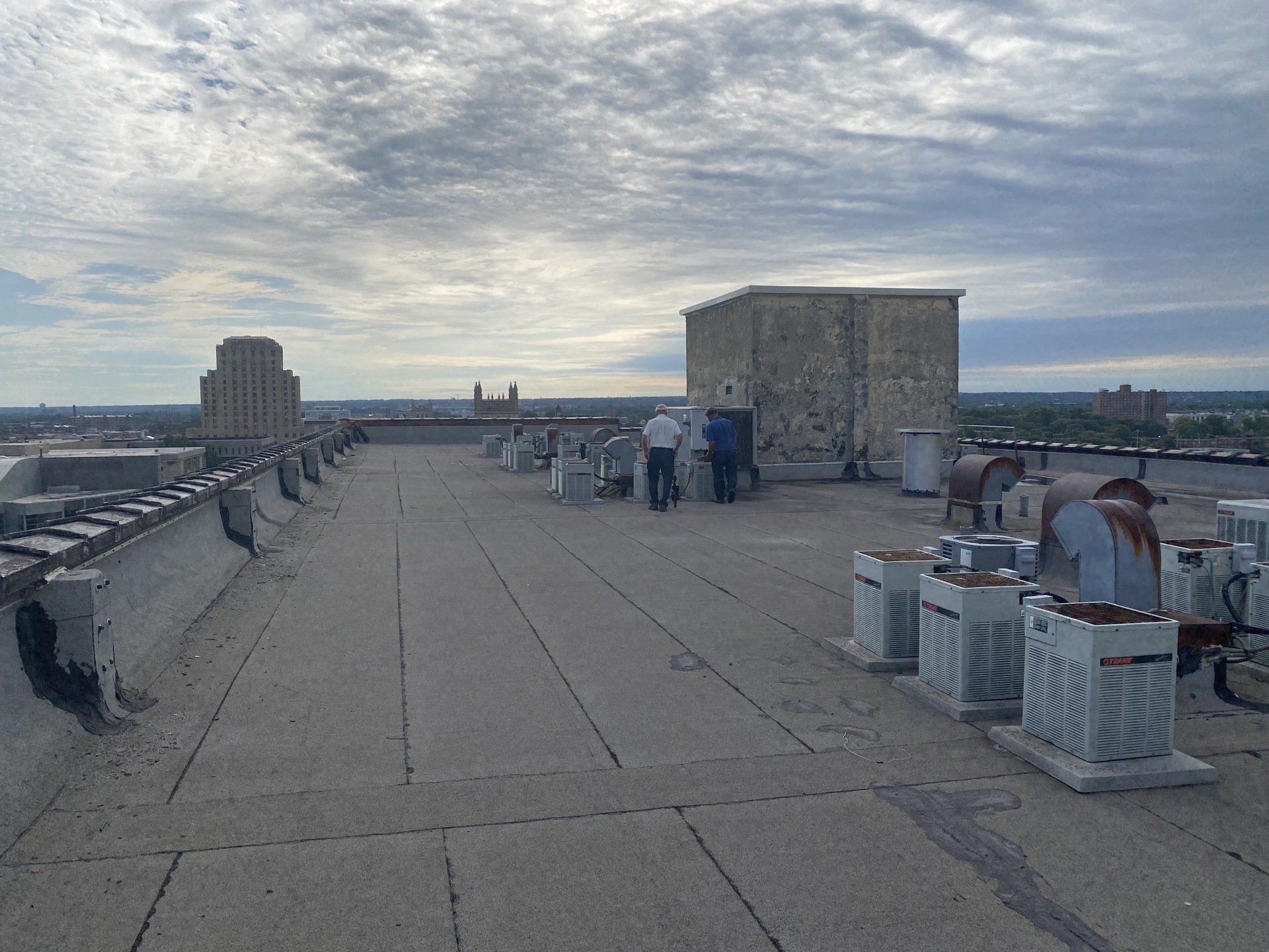 Rooftop with equipment. Two figures near a stone building. Overcast sky above.