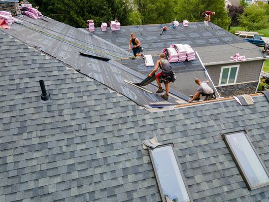 Roofers installing shingles on a house roof.