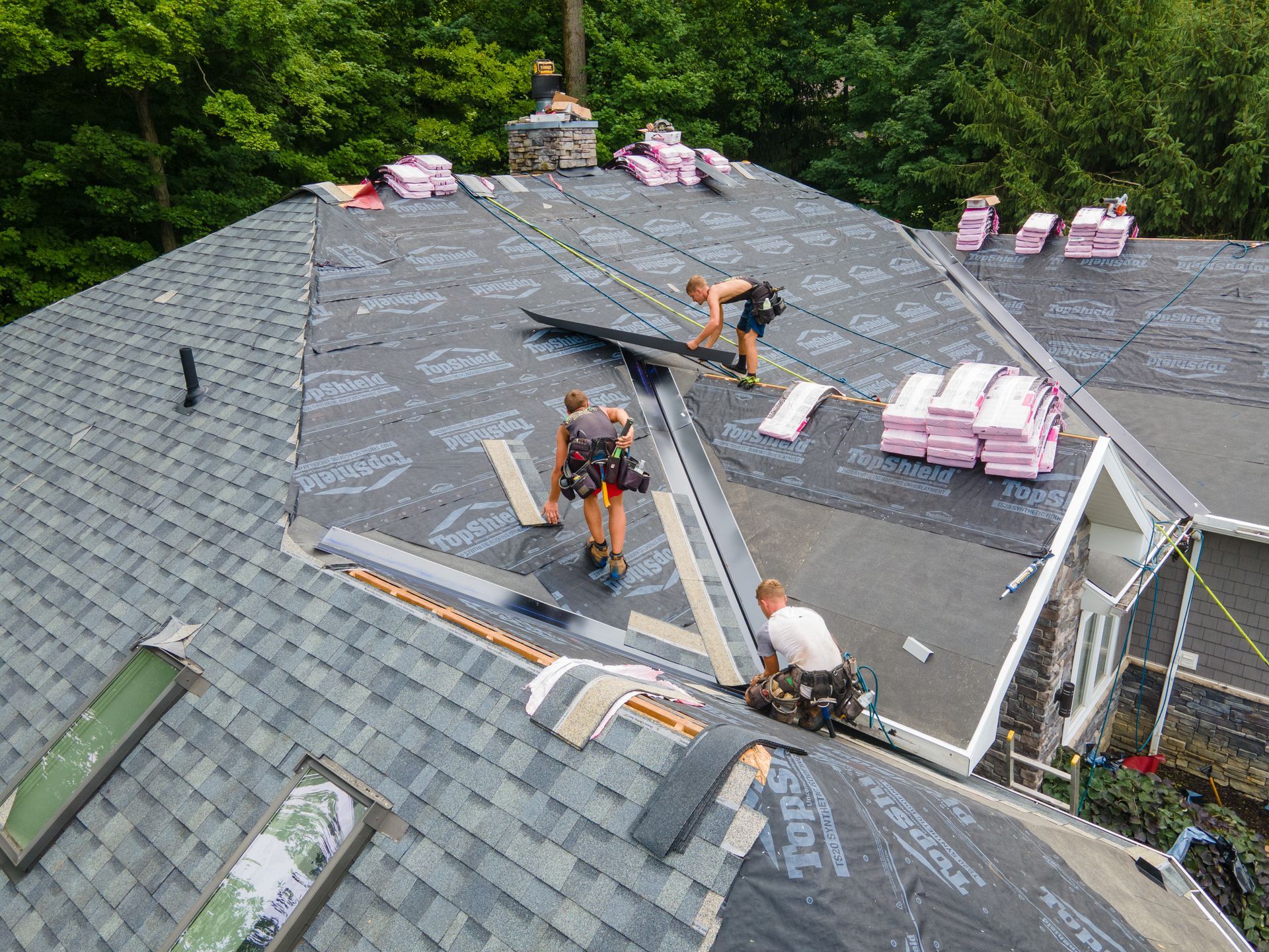 Roofers installing shingles on a house roof, with materials and tools visible.