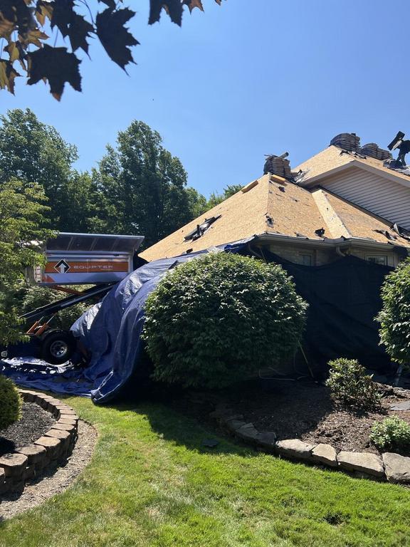 Roof being repaired, partially covered by a tarp. A lift is beside the house.