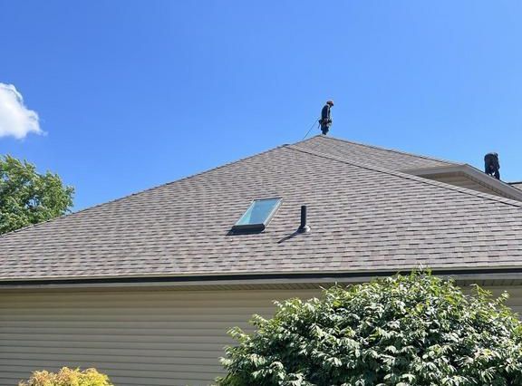 Person on a roof with a hose, cleaning it. Sunny day, blue sky.
