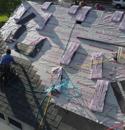 Roofers installing shingles on a house roof, using equipment and materials.
