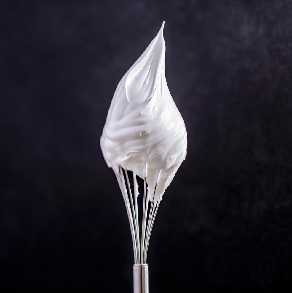 Crème fouettée sur un fouet sur fond noir.