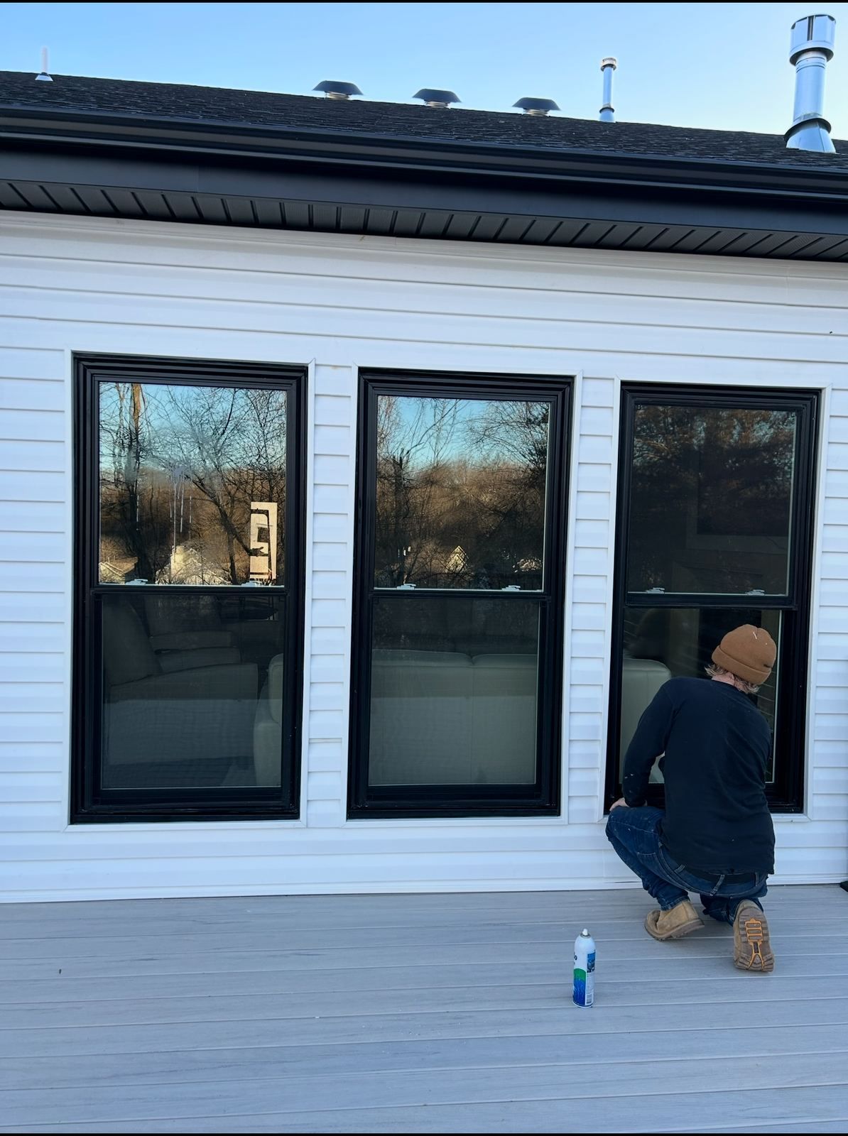 Technician cleaning three new black double-hung windows on white siding