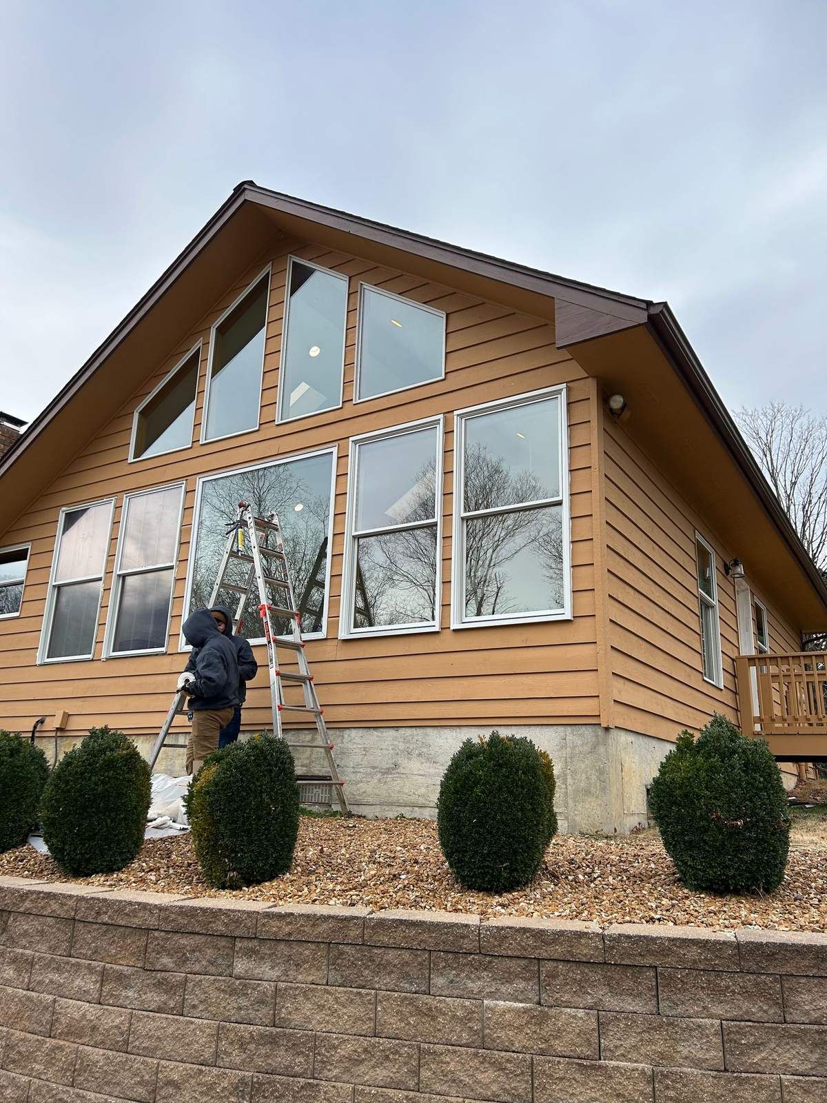 Crew on a ladder working on the large gable windows of a tan-sided house