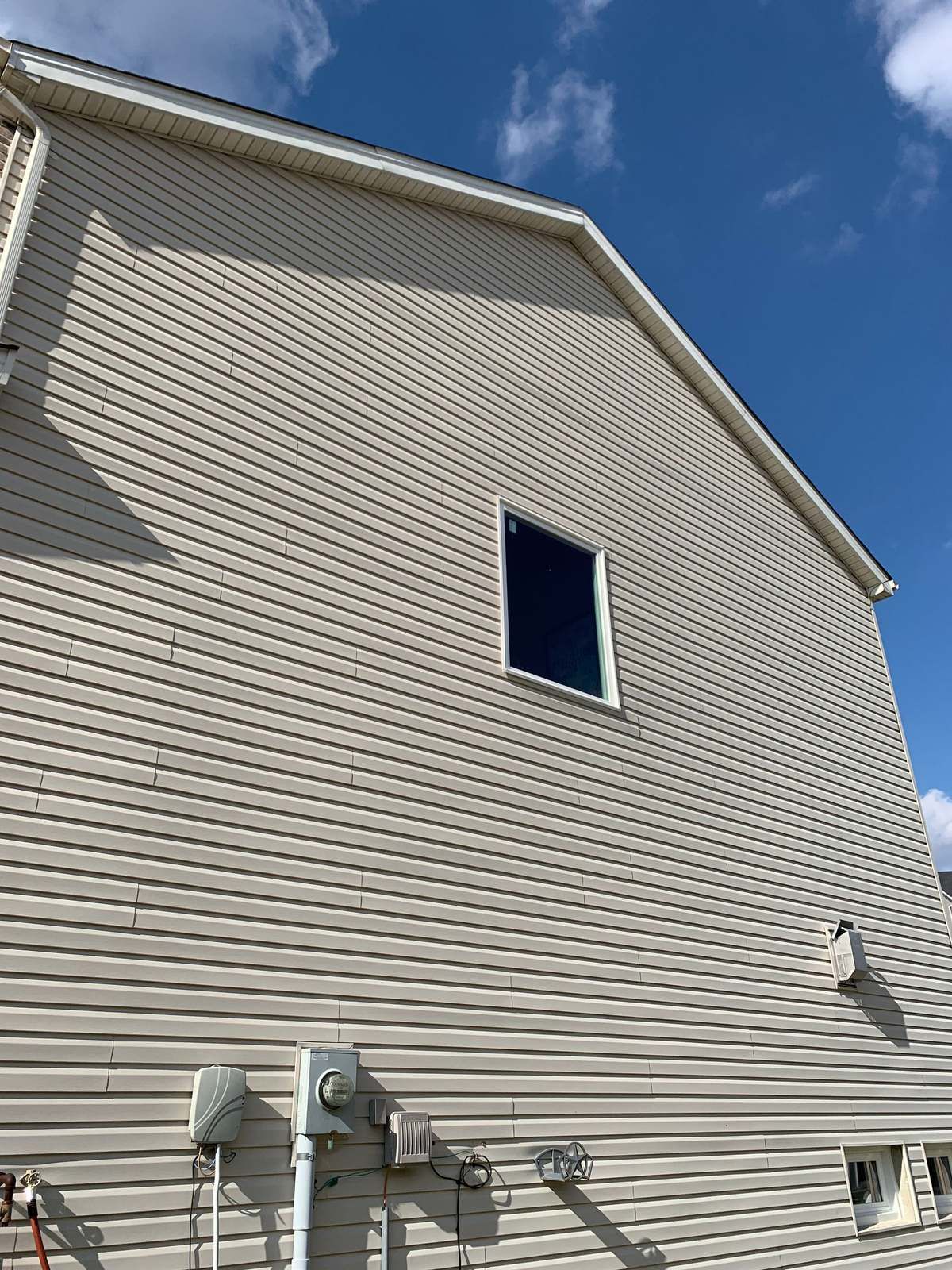 Tan vinyl siding on a two-story gable wall with one window