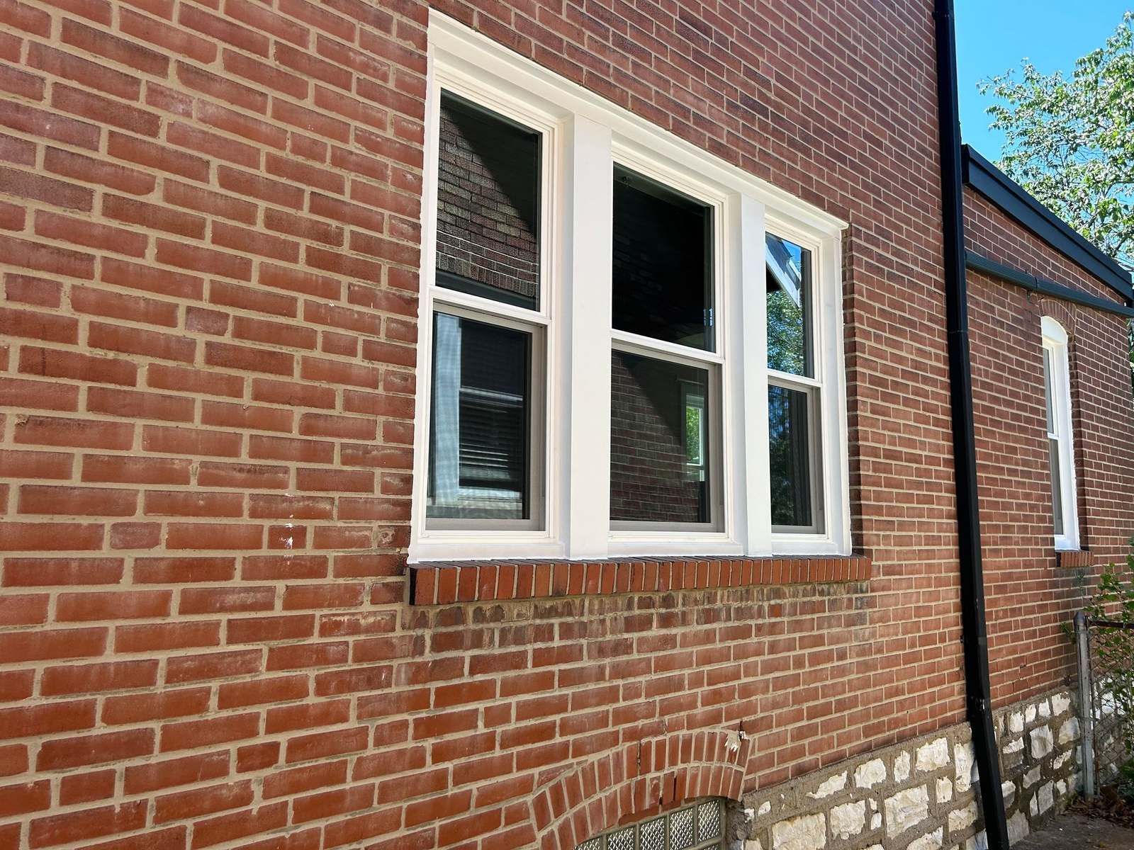 Three white double-hung windows in a red brick wall