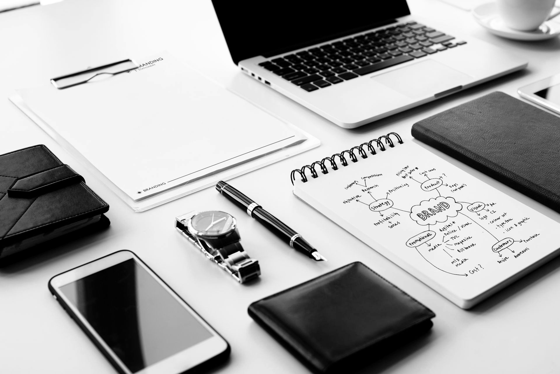 Workspace: Laptop, notebook with diagram, phone, watch, pen, wallet, clipboard, and notepad.