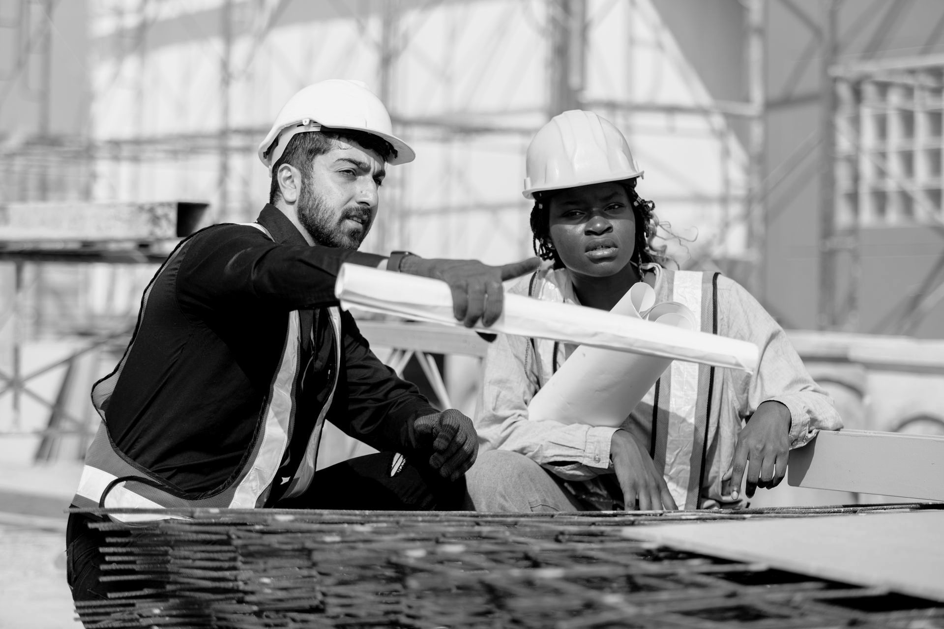 Construction workers reviewing blueprints at a construction site. Man points, woman looks concerned.