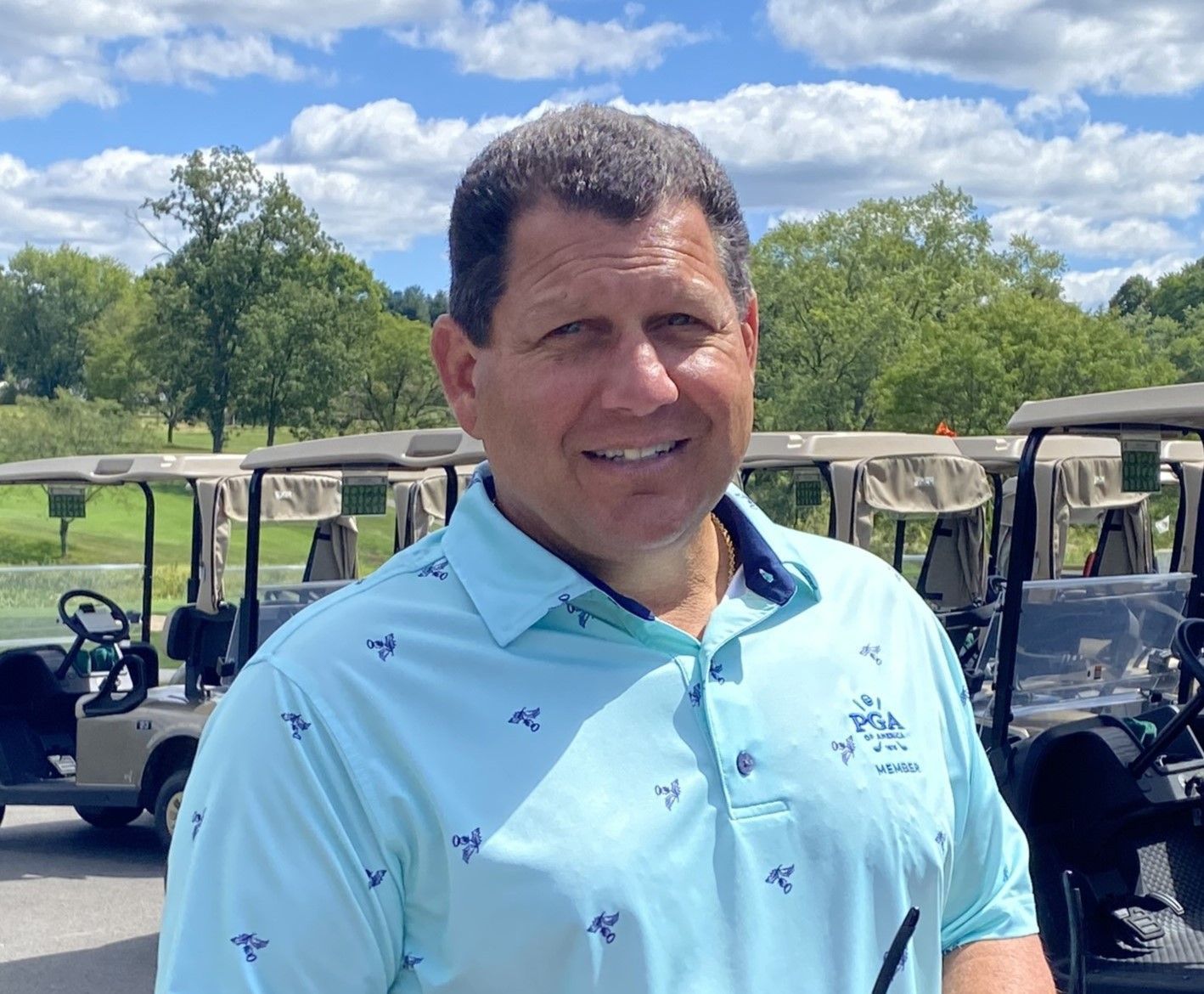 A man in a blue shirt is standing in front of golf carts on a golf course.