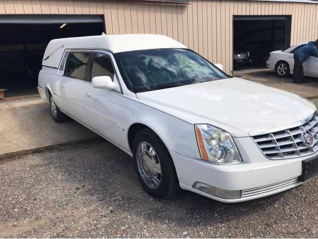 A white cadillac hearse is parked in front of a garage.