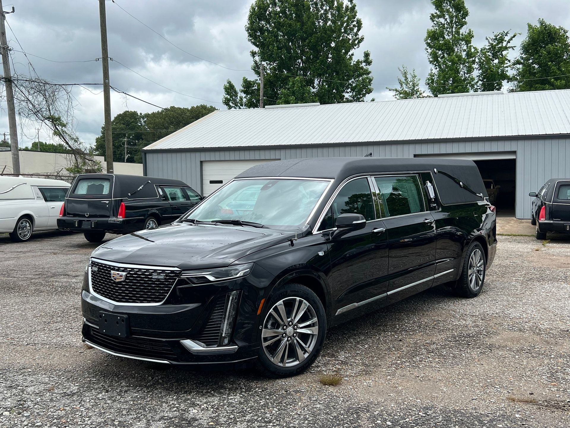 A black hearse is parked in a gravel lot in front of a building.