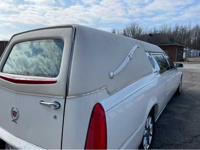 A white cadillac hearse is parked in a parking lot.
