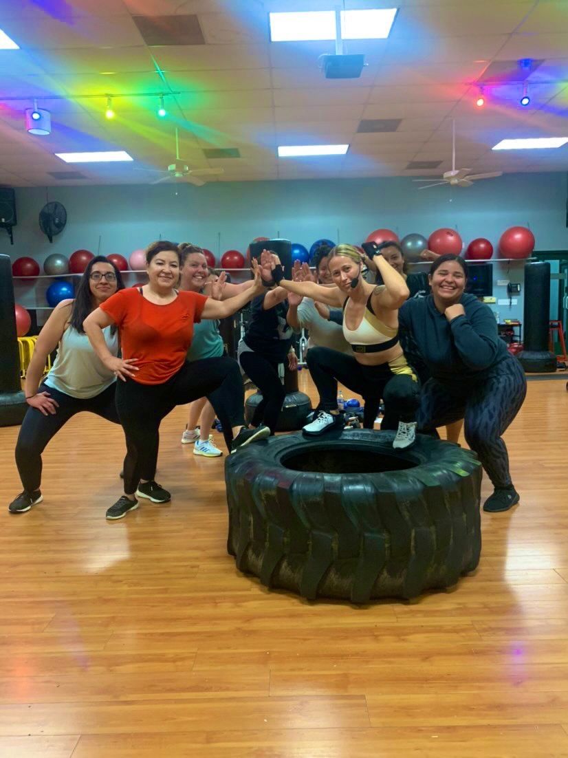 A group of women are posing for a picture in front of a tire in a gym.