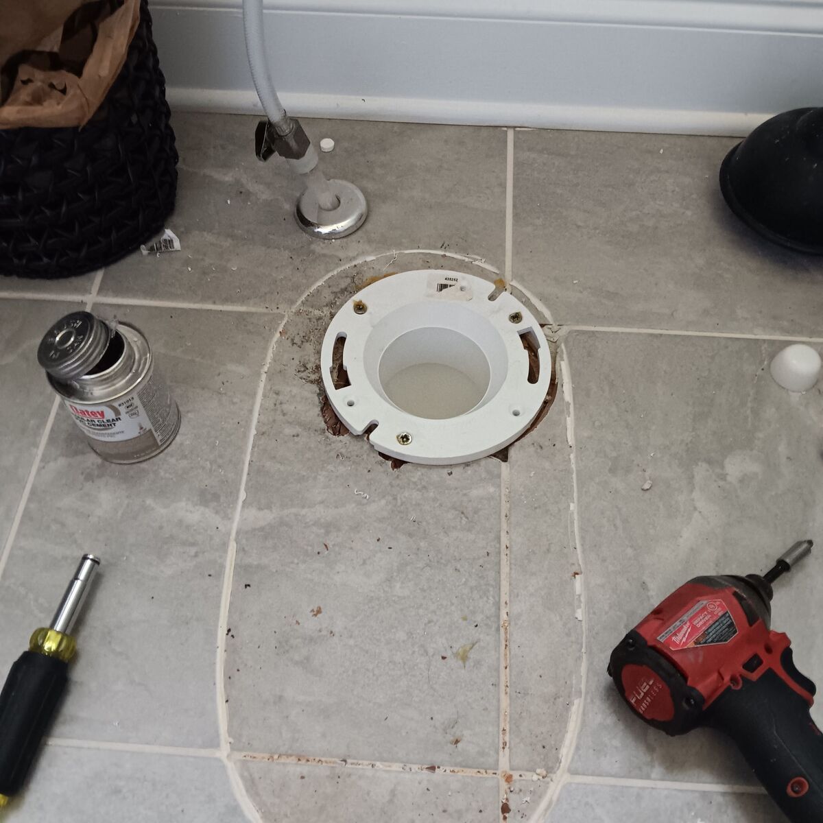 Toilet flange repair in bathroom; tools, plumbing fitting, and floor tiles visible.