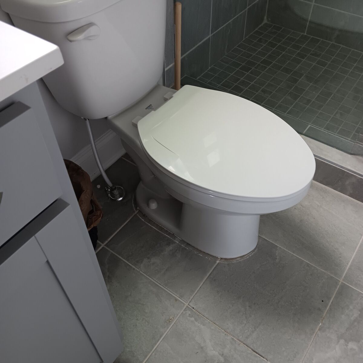 Toilet in a bathroom with gray tile floor, white toilet seat, and gray vanity.
