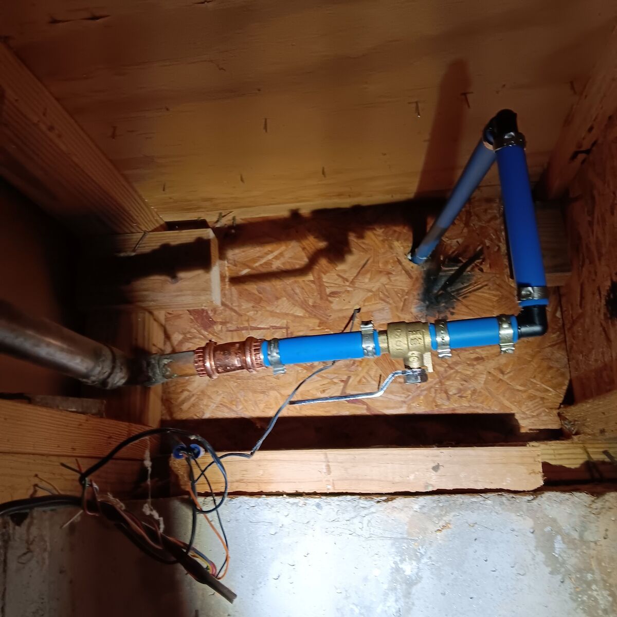 Piping and plumbing connections inside a wooden structure, including copper and blue PEX pipes, and a brass valve.