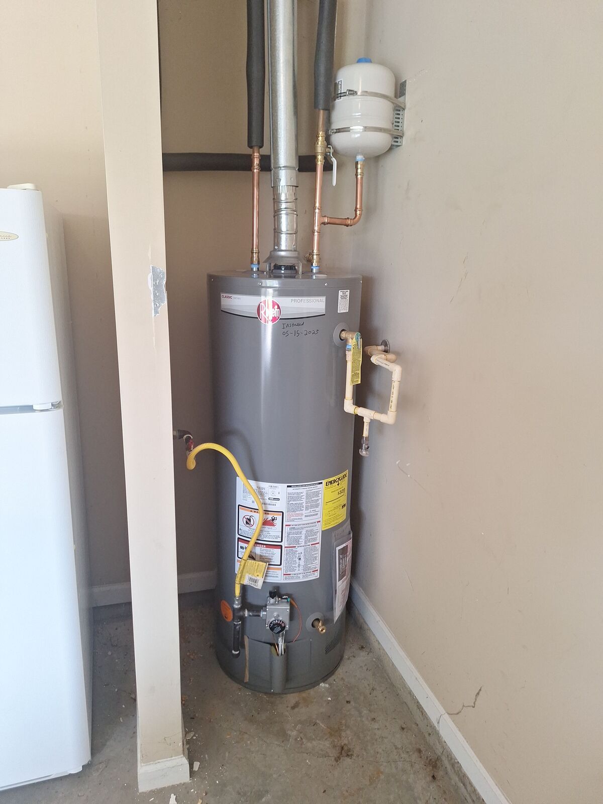 A gray water heater in a corner, with vent pipes and a small expansion tank.