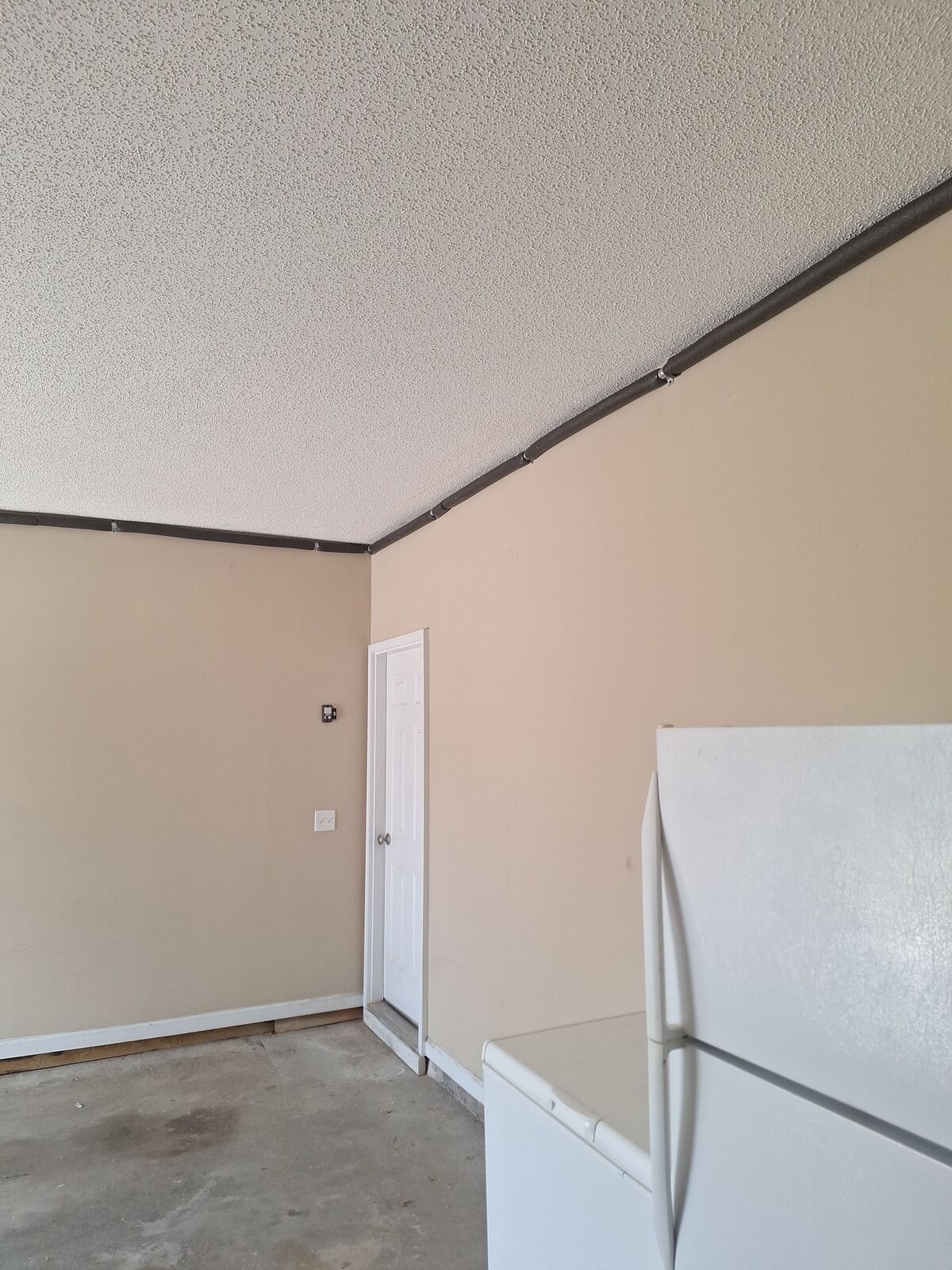 A beige-walled room with a white refrigerator, door, and popcorn ceiling.