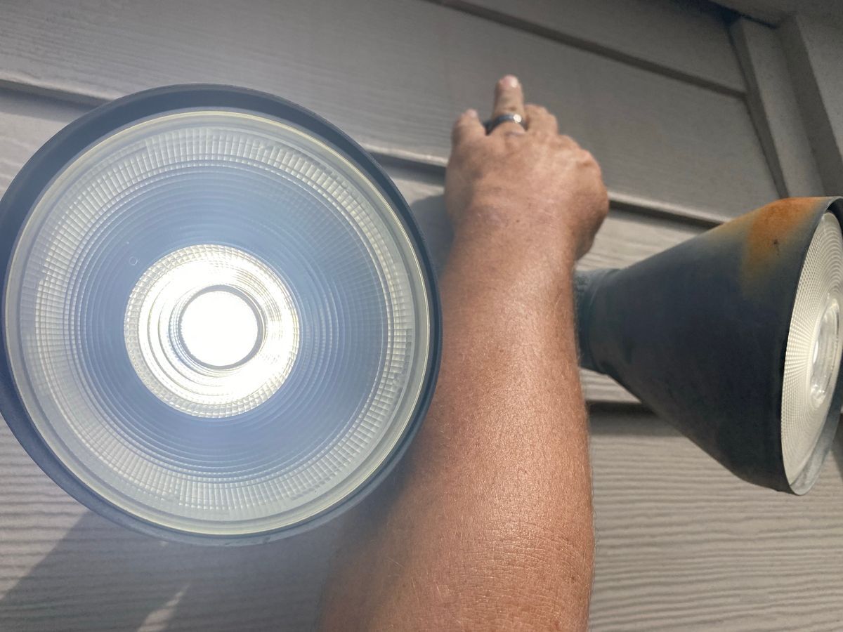 Person adjusting a bright floodlight attached to a gray house siding.