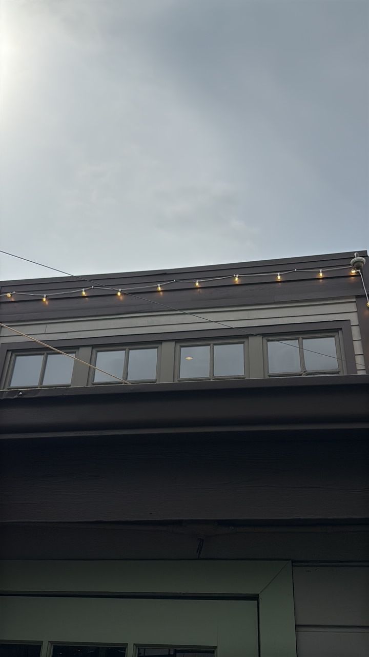 Facade of a building with five windows. Small lights are strung along the roofline against a cloudy sky.