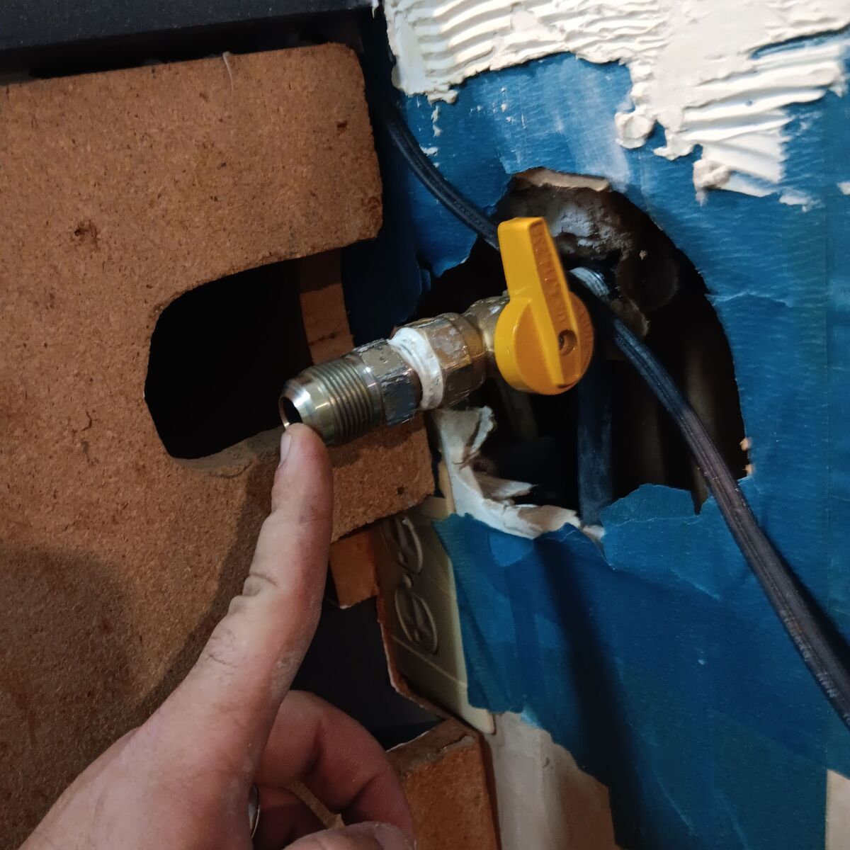 Hand pointing at a gas valve with a yellow handle emerging from a wall.