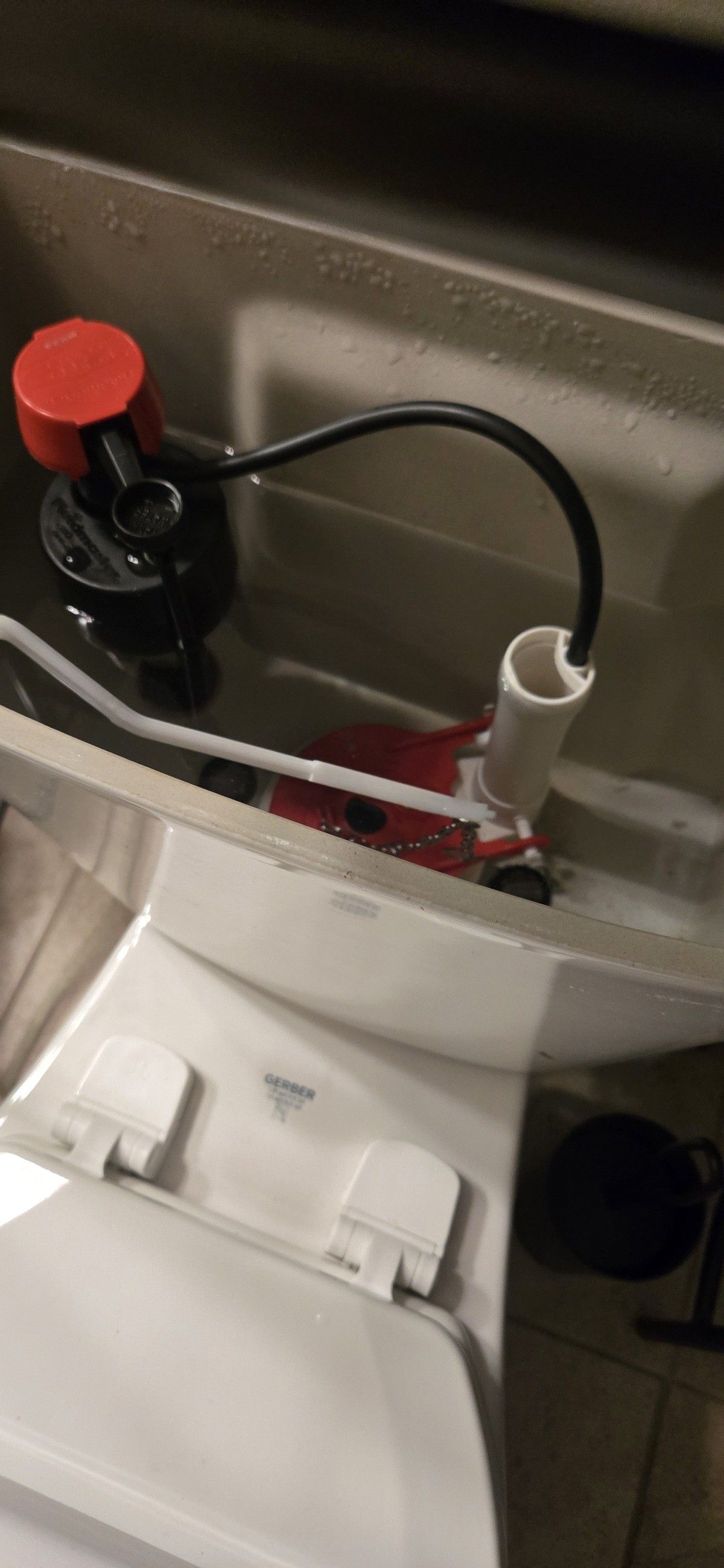 Toilet tank interior with a red and black fill valve, connected by a black tube to a white tube.