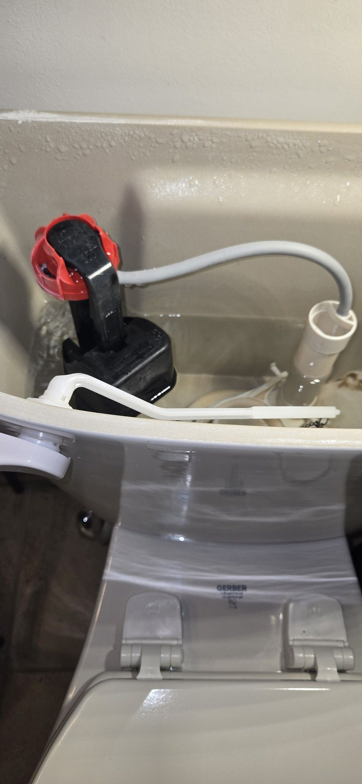 Toilet tank interior with a red and black fill valve, a gray hose, and a white float.